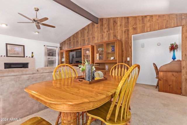 carpeted dining area with wooden walls, vaulted ceiling with beams, and ceiling fan