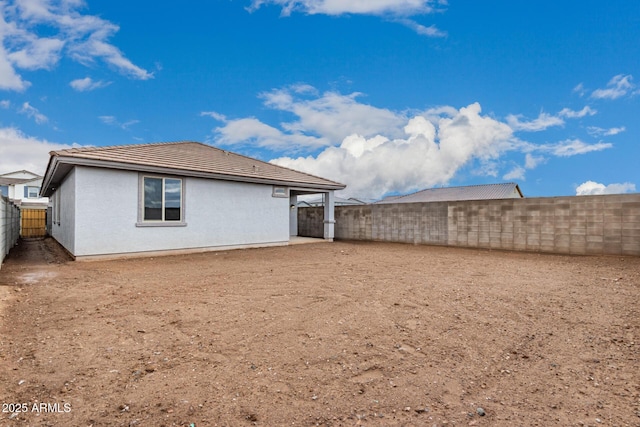 rear view of house with stucco siding, a tiled roof, and a fenced backyard