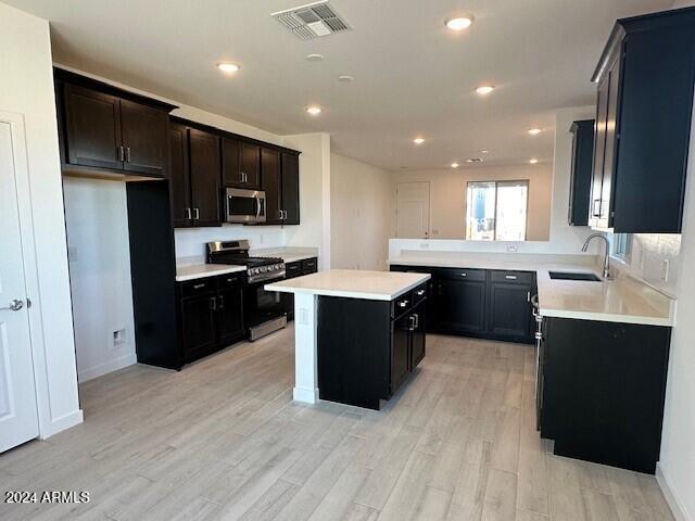 kitchen featuring visible vents, light wood-style flooring, a sink, a center island, and stainless steel appliances