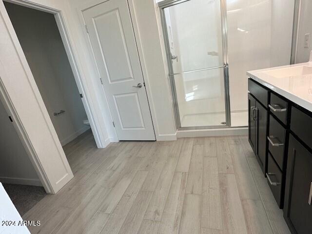 full bath with vanity, wood finished floors, a stall shower, and baseboards