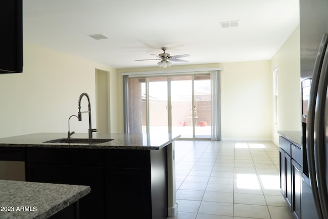 kitchen featuring dark stone countertops, light tile patterned floors, sink, stainless steel fridge, and ceiling fan