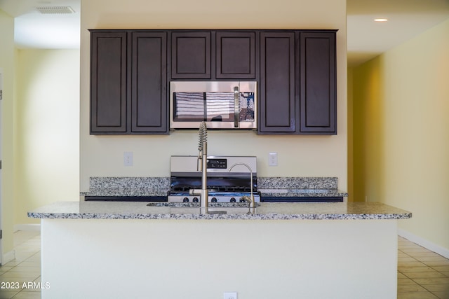 kitchen with appliances with stainless steel finishes, light stone counters, sink, dark brown cabinets, and light tile patterned flooring