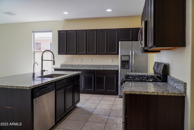 kitchen with light tile patterned floors, an island with sink, sink, appliances with stainless steel finishes, and dark brown cabinetry