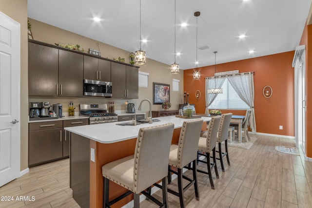 kitchen featuring appliances with stainless steel finishes, light hardwood / wood-style flooring, decorative light fixtures, a center island with sink, and sink