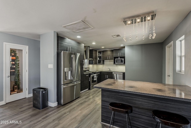 8137 E Indian School Rd, Scottsdale, AZ 85251 - kitchen featuring stainless steel appliances, a breakfast bar, wall chimney exhaust hood, wood finished floors, and tasteful backsplash