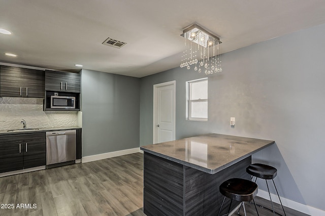8137 E Indian School Rd, Scottsdale, AZ 85251 - kitchen with appliances with stainless steel finishes, a kitchen bar, dark wood finished floors, backsplash, and recessed lighting