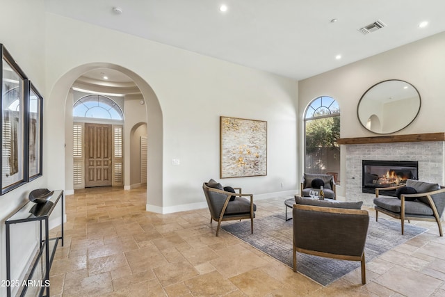 living room featuring a towering ceiling, a brick fireplace, and a wealth of natural light