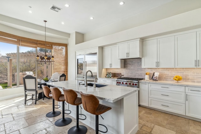 kitchen featuring white cabinetry, an island with sink, sink, premium appliances, and hanging light fixtures