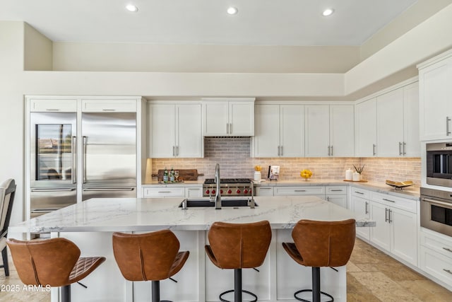 kitchen with a kitchen island with sink, white cabinets, light stone counters, and stainless steel built in fridge