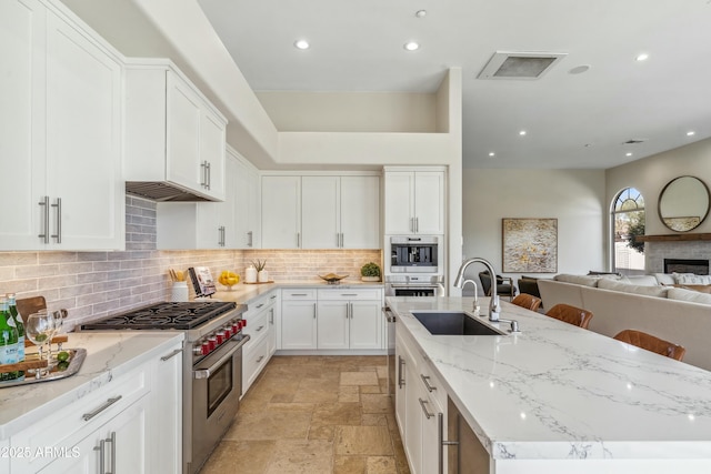 kitchen featuring a breakfast bar, sink, white cabinetry, light stone counters, and stainless steel appliances