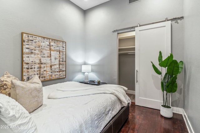 bedroom with a walk in closet, a barn door, dark hardwood / wood-style floors, and a closet