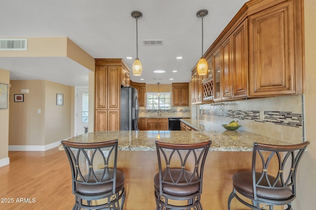 kitchen with stainless steel fridge, black dishwasher, kitchen peninsula, pendant lighting, and light stone countertops