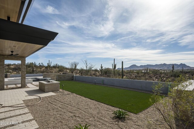 view of yard with ceiling fan, an outdoor fire pit, a mountain view, and a patio