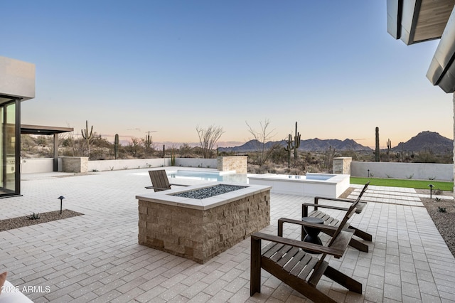 patio terrace at dusk featuring a hot tub, a mountain view, and an outdoor fire pit