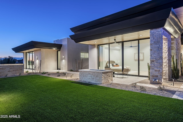 back house at dusk featuring a lawn, ceiling fan, and a patio area