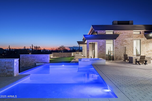 pool at dusk featuring a patio area and a hot tub