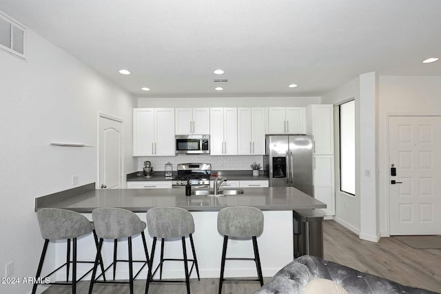 kitchen with white cabinets, dark hardwood / wood-style flooring, a kitchen bar, and stainless steel appliances