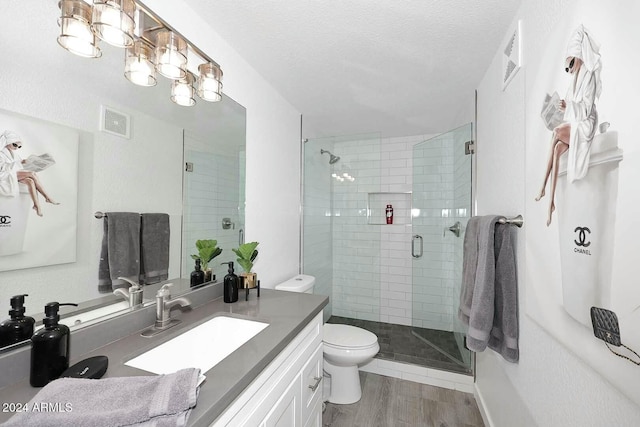 bathroom featuring vanity, a textured ceiling, hardwood / wood-style flooring, toilet, and a shower with shower door