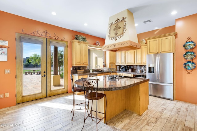 kitchen with light brown cabinets, a center island, stainless steel fridge, a kitchen bar, and decorative backsplash