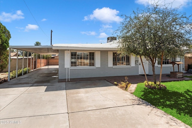 view of front of home featuring brick siding, a front lawn, fence, a carport, and driveway