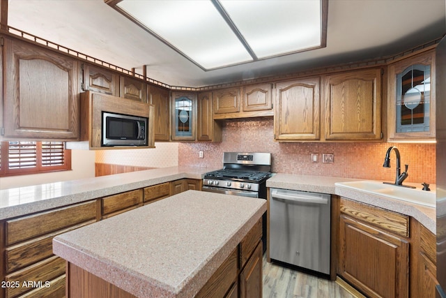 kitchen with a sink, tasteful backsplash, stainless steel appliances, light countertops, and glass insert cabinets