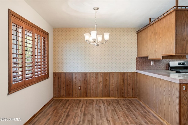 unfurnished dining area featuring wallpapered walls, an inviting chandelier, wood finished floors, and a wainscoted wall