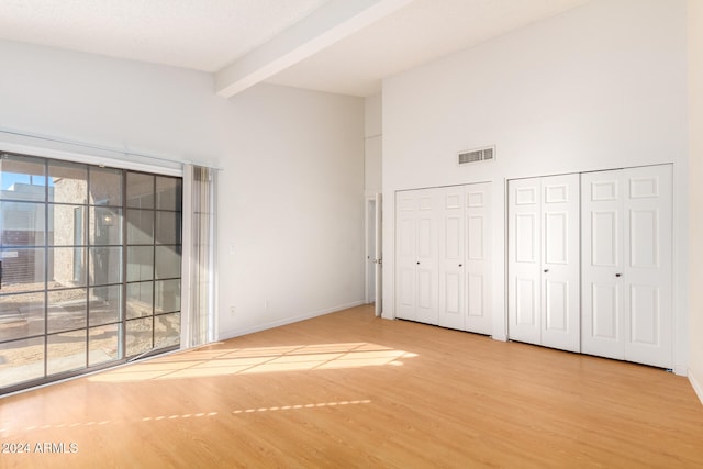 unfurnished bedroom with lofted ceiling with beams, light hardwood / wood-style flooring, and multiple closets