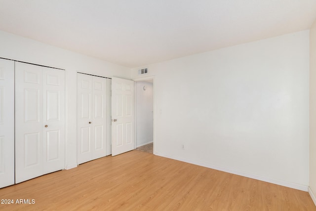 unfurnished bedroom featuring multiple closets and light wood-type flooring