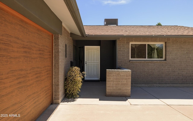 8502 E Rose Ln, Scottsdale, AZ 85250 - view of exterior entry with brick siding, roof with shingles, a patio area, and central air condition unit