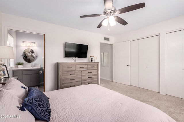 carpeted bedroom featuring two closets, connected bathroom, and ceiling fan