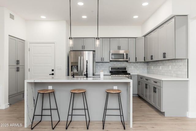 kitchen featuring gray cabinets, a kitchen bar, hanging light fixtures, a kitchen island with sink, and stainless steel appliances