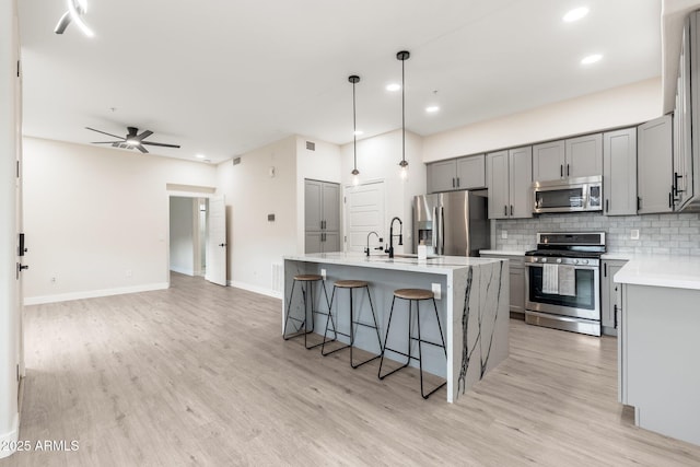 kitchen featuring gray cabinetry, hanging light fixtures, backsplash, stainless steel appliances, and an island with sink