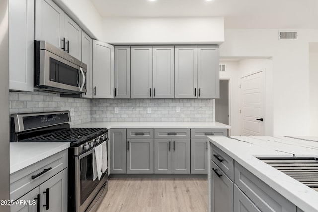 kitchen featuring tasteful backsplash, appliances with stainless steel finishes, gray cabinets, and light stone countertops