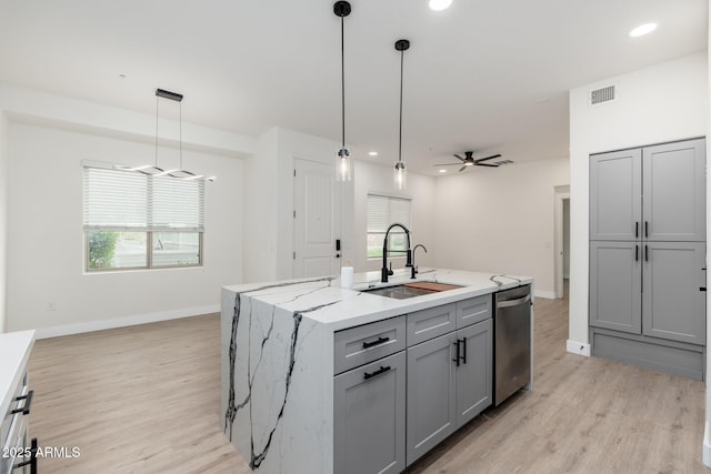 kitchen featuring stainless steel dishwasher, decorative light fixtures, an island with sink, and gray cabinetry