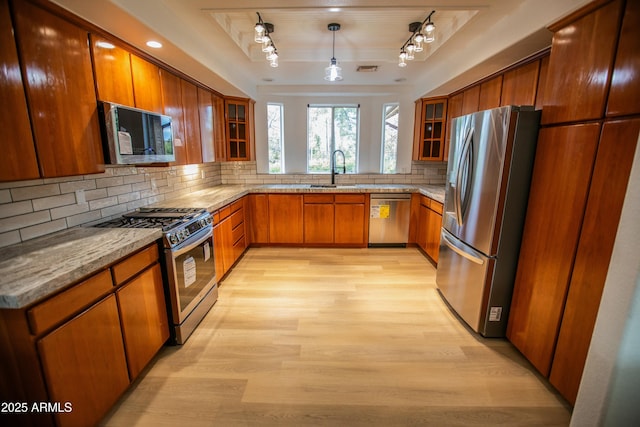 kitchen featuring brown cabinets, a sink, light wood-style floors, appliances with stainless steel finishes, and a raised ceiling