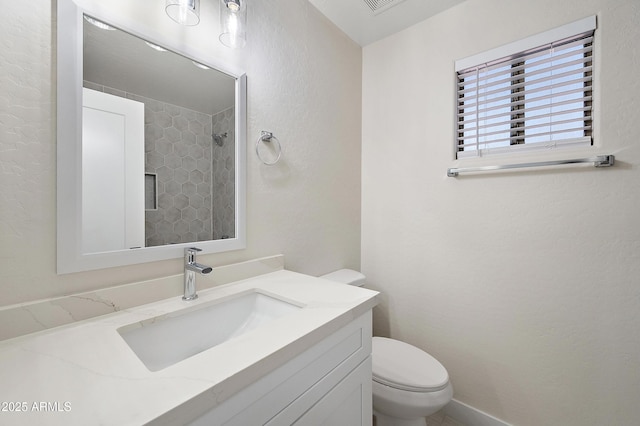 bathroom with toilet, vanity, and a tile shower