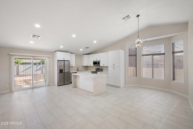 kitchen with white cabinetry, appliances with stainless steel finishes, decorative light fixtures, light stone countertops, and vaulted ceiling