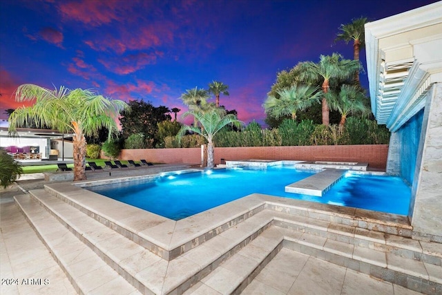 pool at dusk featuring pool water feature, an in ground hot tub, and a patio area