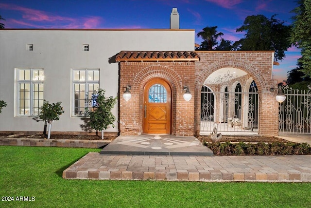 exterior entry at dusk featuring a lawn