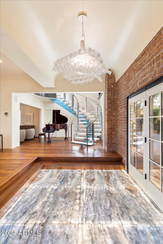 foyer entrance featuring a notable chandelier, vaulted ceiling, hardwood / wood-style floors, and brick wall