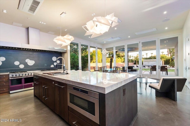 kitchen with dark brown cabinets, sink, an island with sink, backsplash, and decorative light fixtures