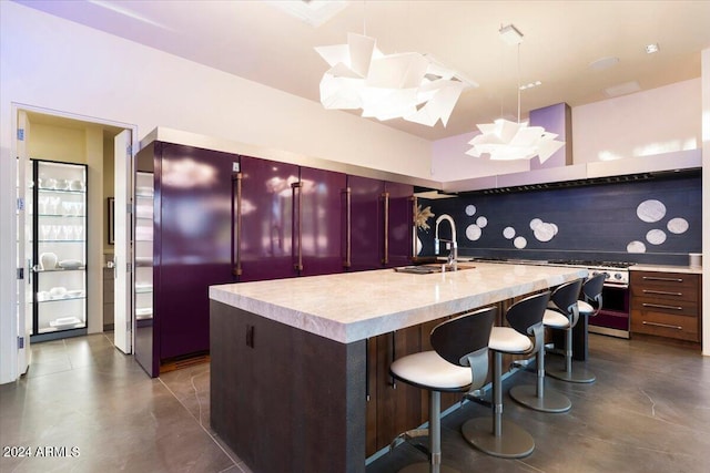 kitchen featuring sink, tasteful backsplash, a center island with sink, decorative light fixtures, and a breakfast bar