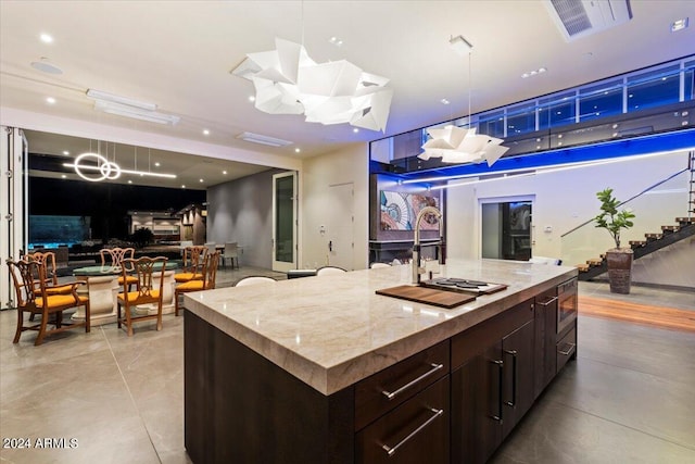 kitchen with light stone countertops, dark brown cabinetry, and a kitchen island with sink