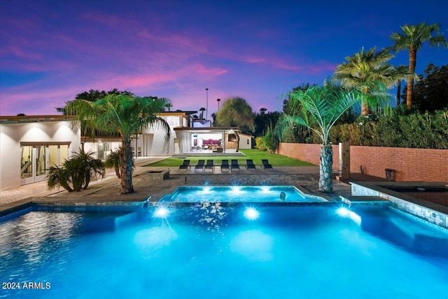 pool at dusk featuring an in ground hot tub and a patio area