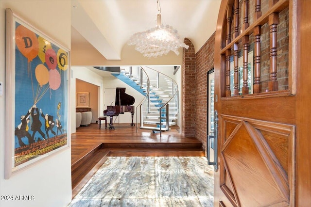 foyer featuring a notable chandelier, wood-type flooring, lofted ceiling, and brick wall