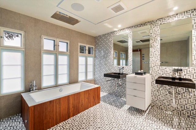 bathroom with tile walls, tile patterned flooring, a tub, and vanity