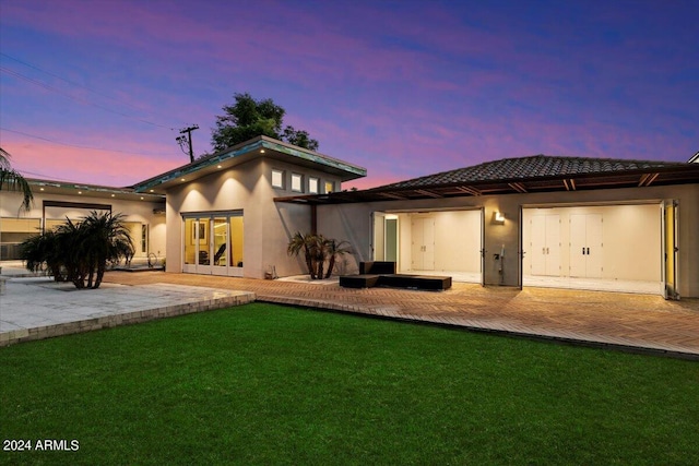 back house at dusk with a lawn and a patio area