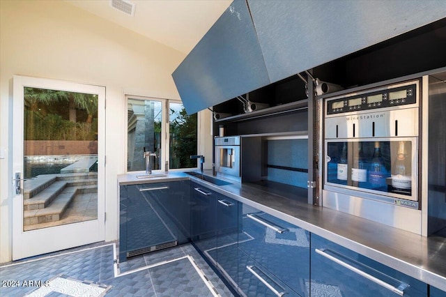 kitchen featuring oven, vaulted ceiling, sink, and stainless steel counters