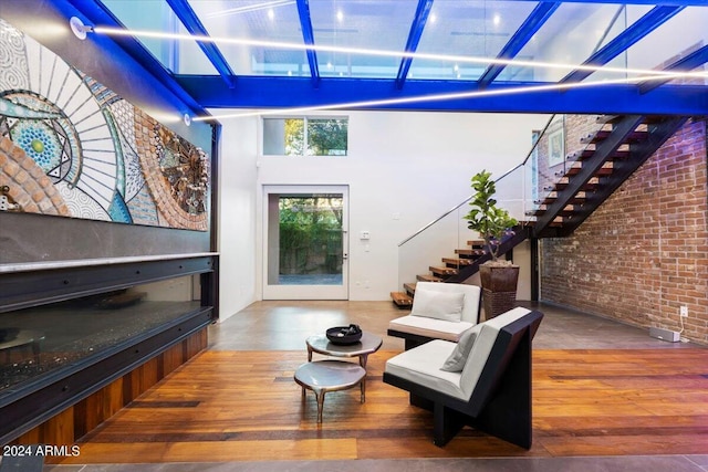 living area featuring a towering ceiling, brick wall, and hardwood / wood-style floors