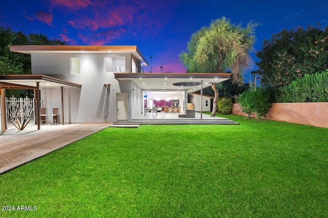 back house at dusk with a patio and a yard